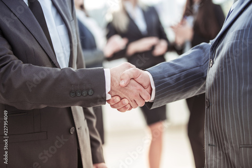 concept of cooperation - handshake of business partners on the background of the employees in the office