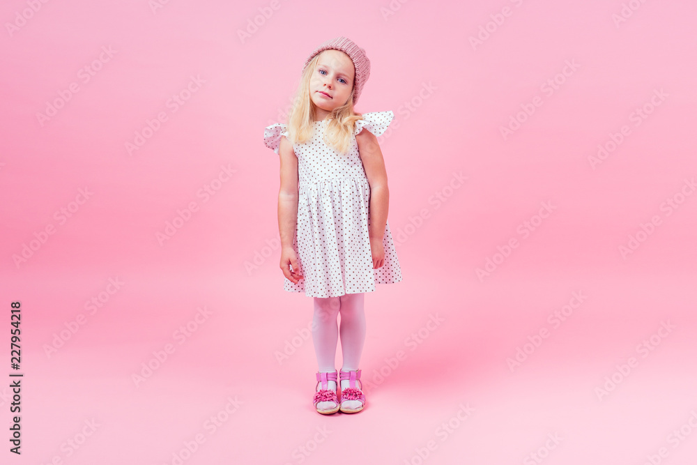 Full body portrait of adorable little girl blonde girl blue eyes model in beige knitted pink hat in white princess dress in peas autumnal springtime season in studio shot on pink background Full body portrait of adorable little girl blonde girl blue eyes model in beige knitted pink hat in white princess dress in peas autumnal springtime season in studio shot on pink background