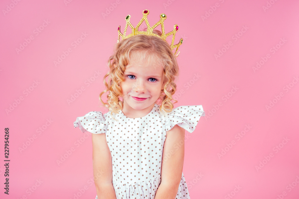 little girl beauty queen blue eyes, curls blonde hairstyle with a tiara crown on her head in a cute white dress in peas posing in the studio on a pink background.birthday celebration,Beauty contest little girl beauty queen blue eyes, curls blonde hairstyle with a tiara crown on her head in a cute white dress in peas posing in the studio on a pink background.birthday celebration,Beauty contest