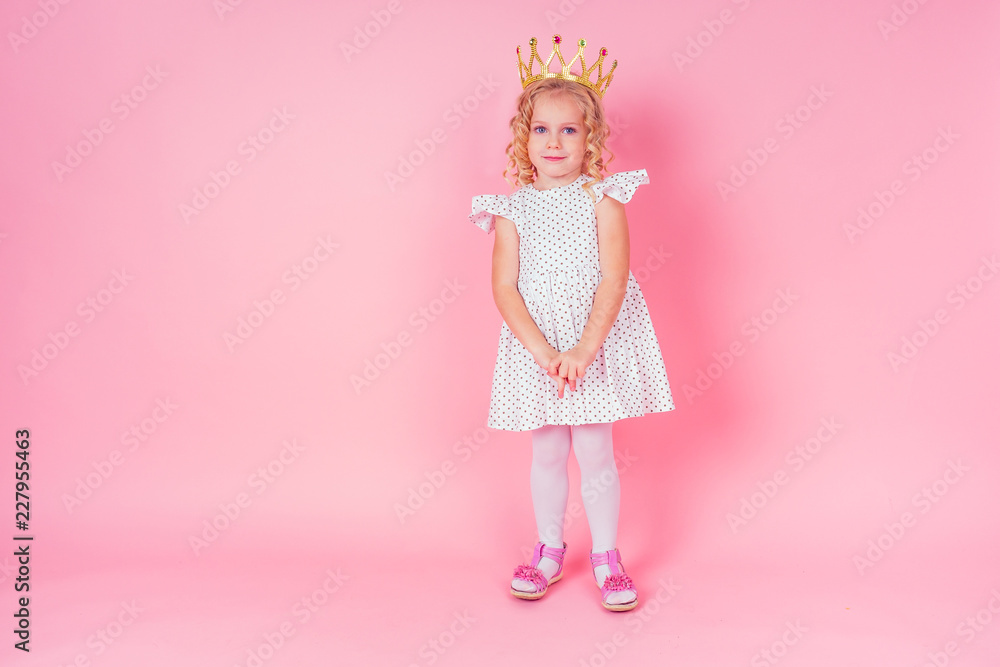 Beautiful queen in gold crown.little shopping girl in a princess fashion dress. Pretty child preparing for a birthday Easter party on a pink background in the studio. Beautiful queen in gold crown.little shopping girl in a princess fashion dress. Pretty child preparing for a birthday Easter party on a pink background in the studio.