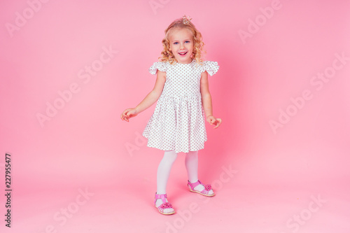 Beautiful queen in gold crown.little shopping girl in a princess fashion dress. Pretty child preparing for a birthday Easter party on a pink background in the studio.