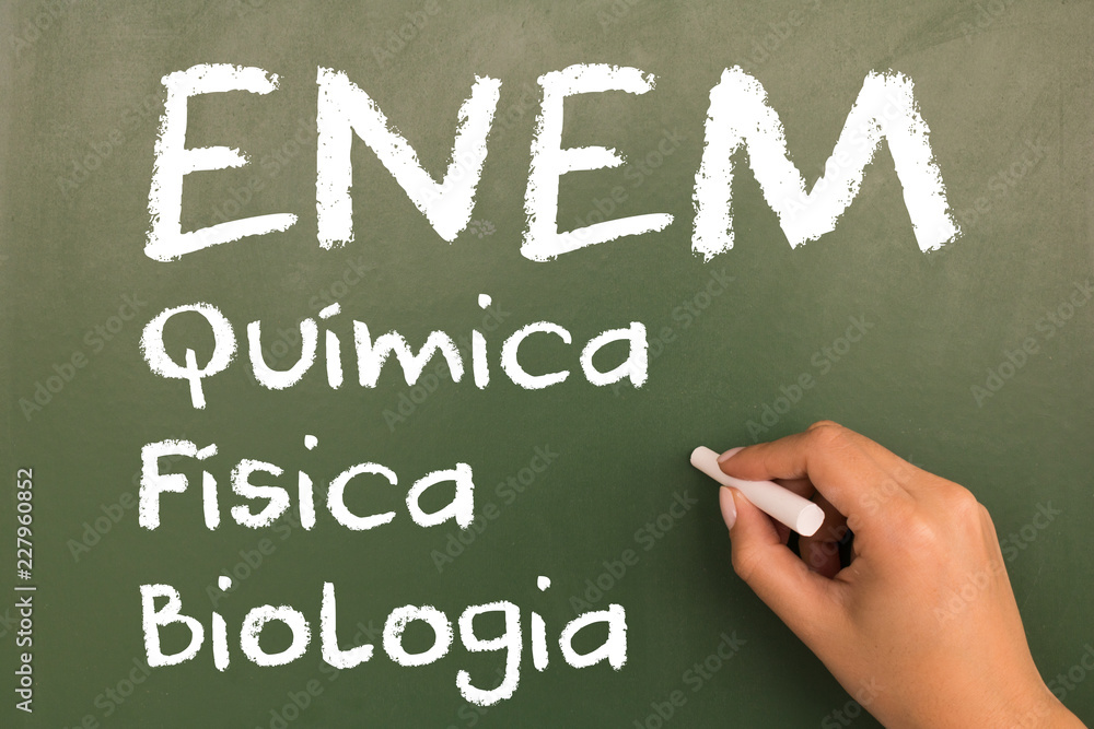 Female hand writing with chalk on empty green chalkboard. (translation portuguese: ENEM - National High School Exam Brazil - chemistry, physics, biology)