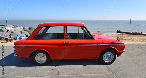 Classic Red Hillman Imp Motor Car parked on seafront promenade.