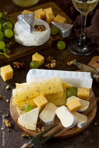 Cheese plate with grapes, wine glass and nuts on dark rustic wooden table.