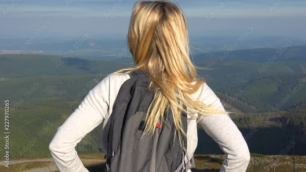 A young beautiful woman stands on a hilltop and looks around at a mountainous landscape A young beautiful woman stands on a hilltop and looks around at a mountainous landscape