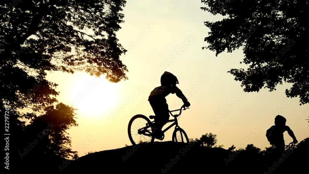 Childrens cycling,Ride up the mound Between two large trees and the sun shines down.Concept Silhouette stay. Childrens cycling,Ride up the mound Between two large trees and the sun shines down.Concept Silhouette stay.