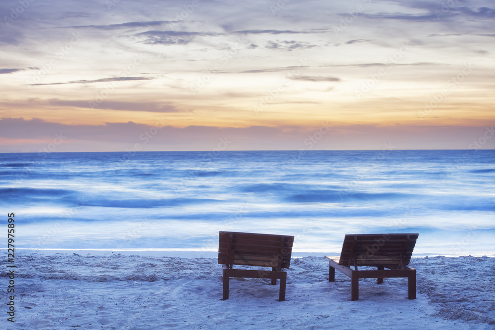 Moody sunset beach with two sunbeds and blurred sea Moody sunset beach with two sunbeds and blurred sea