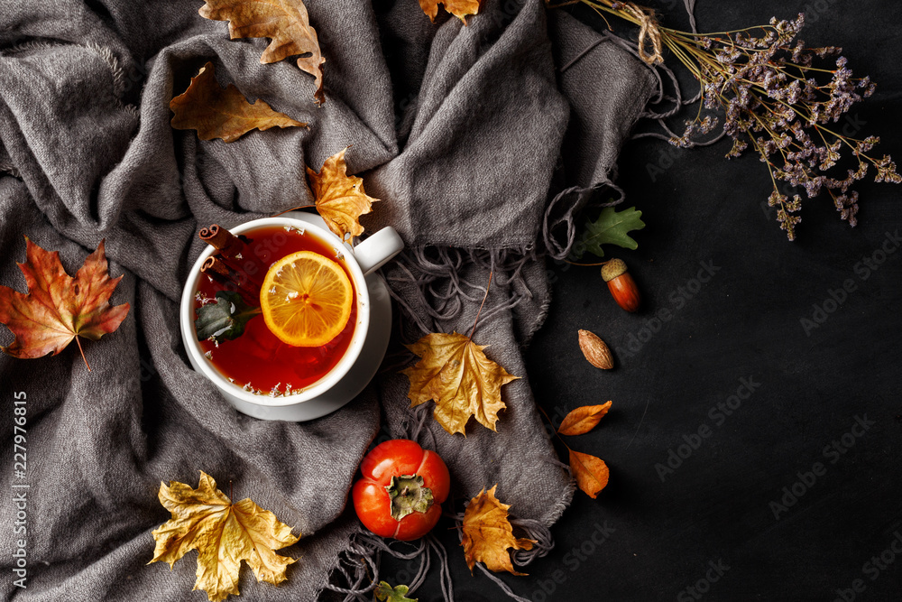 Autumn composition. A cup of fragrant tea with lemon on a dark table with autumn leaves and flowers.