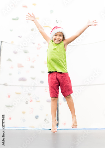 Fototapeta Naklejka Na Ścianę i Meble -  Little boy with Santa hat jumping on trampoline