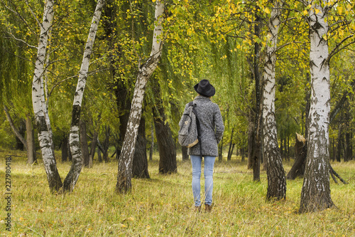 Girl in a hat with a backpack standing in the autumn forest. Back view © somemeans