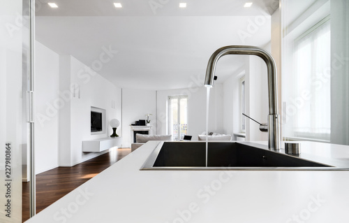 modern kitchen interiors in the foreground the integrated steel sink and the chrome faucet that overlooking on the living area photo