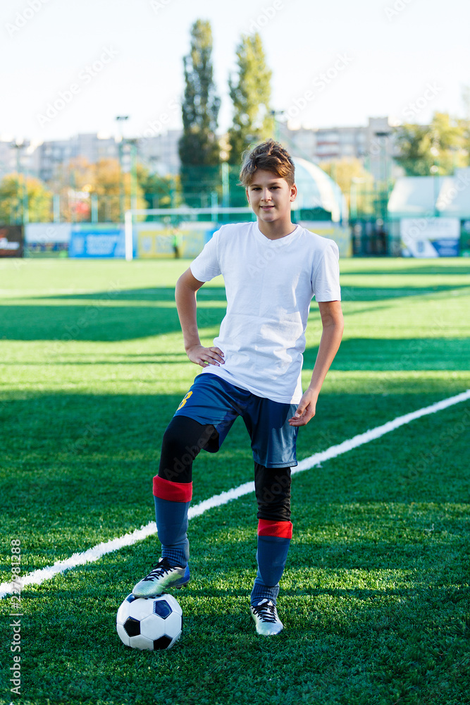 cute young boy in white blue sportswear stands next to classical black and  white football ball on the stadium field. Soccer game, training, hobby  concept. Stock Photo | Adobe Stock