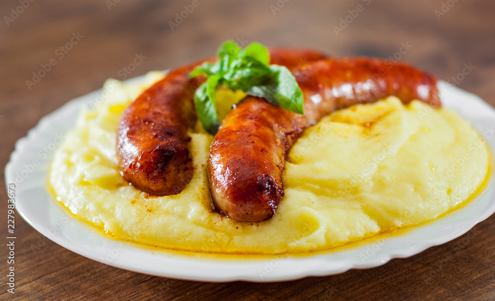fried meat sausages with mashed potatoes in white plate on wooden table background
