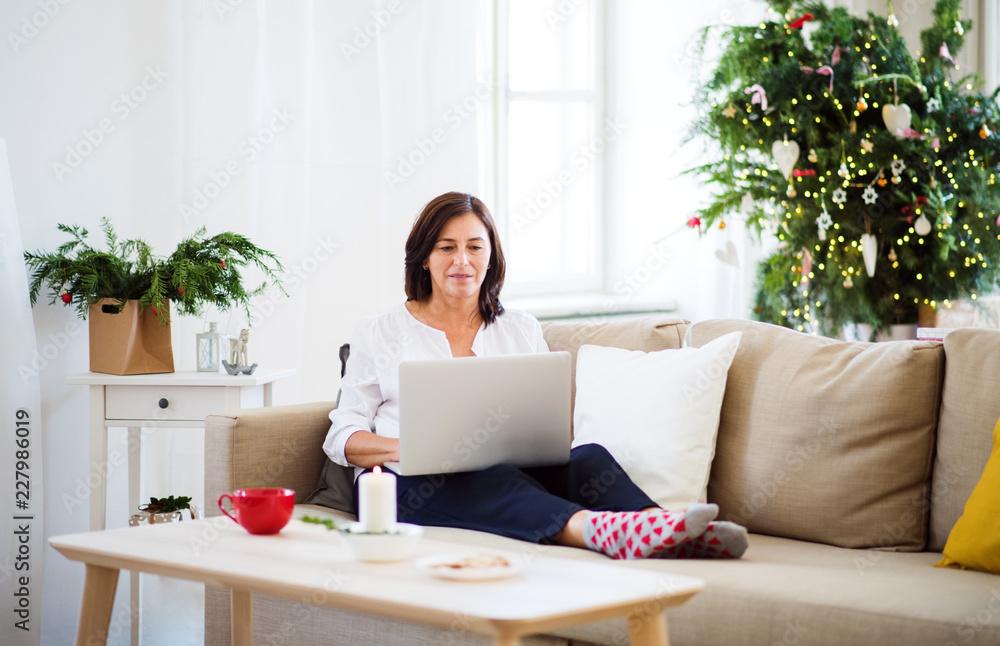 A senior woman with laptop sitting on a sofa at home at Christmas time.