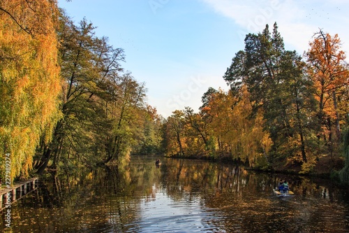 Ukraine. Kyiv. Pushcha Voditsa. Autumn landscape with trees reflecting in the water of the lake and people boating.