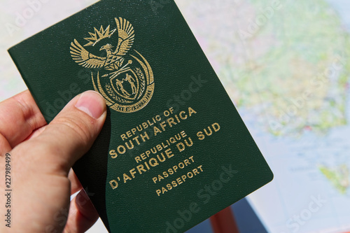 A South African travel passport in a man's hand with map in the background. This image can be used to represent emigration or travel planning. This image has selective focusing. 