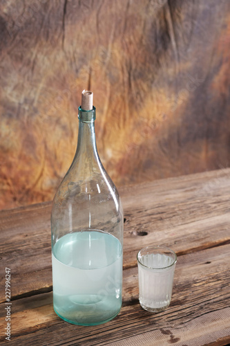 The bottle and glass of moonshine on the old wooden table photo