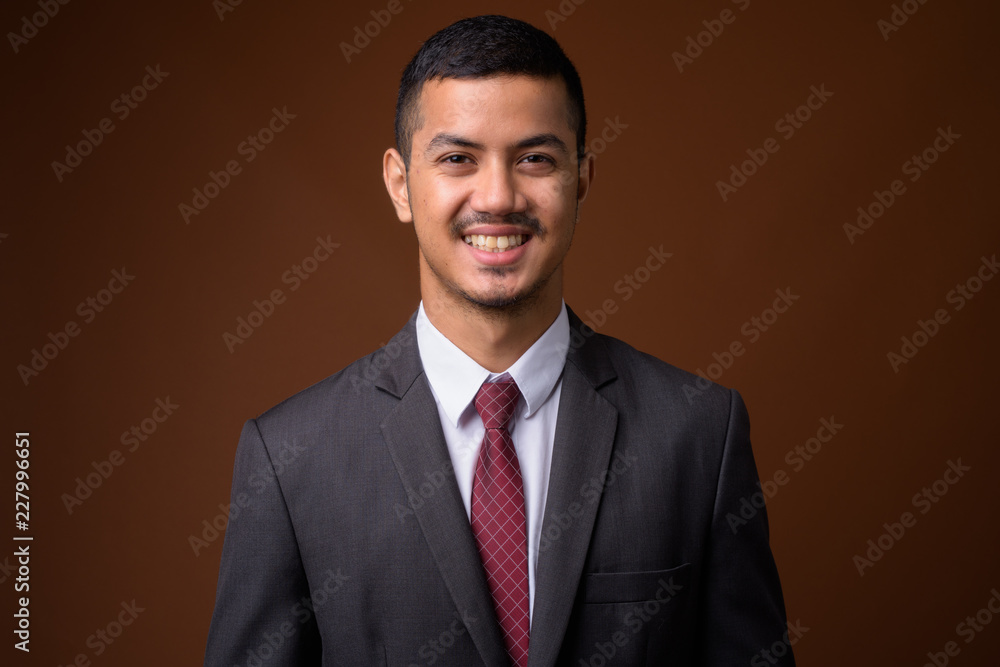 Young multi-ethnic Asian businessman against brown background Young multi-ethnic Asian businessman against brown background