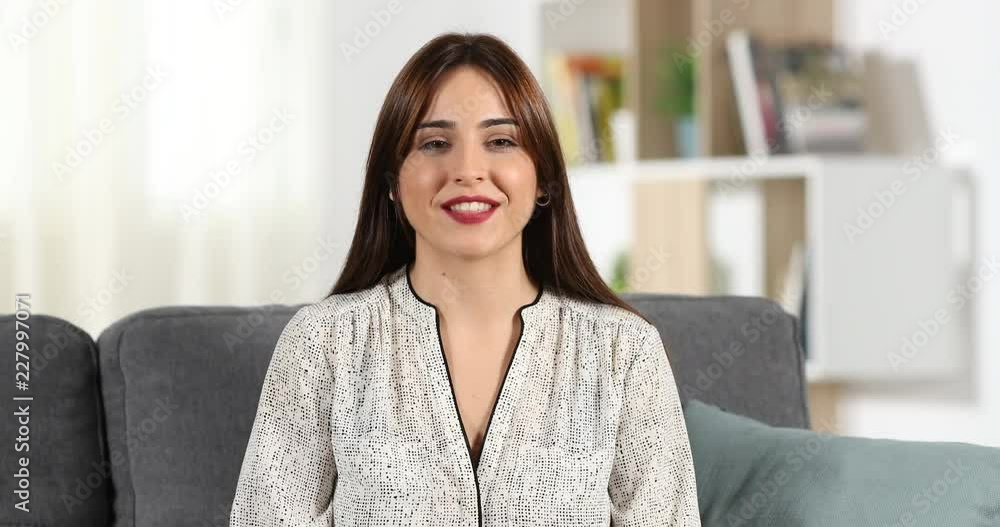 Front view of a happy woman talking to camera sitting on a couch at home Front view of a happy woman talking to camera sitting on a couch at home