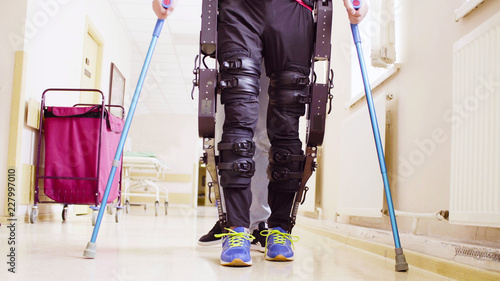 Legs of disable man in the robotic exoskeleton walking through the corridor of the rehabilitation clinic. Doctor helping him. photo