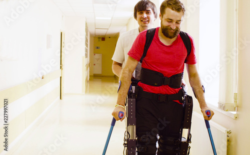 Young disable man in the robotic exoskeleton sitting in wheelchair in the rehabilitation clinic photo