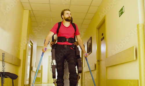 Young disable man in the robotic exoskeleton sitting in wheelchair in the rehabilitation clinic