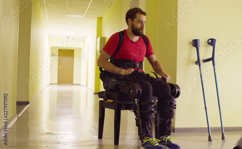 Bild auf Leinwand Disable man in the robotic exoskeleton sitting on the bench and taking off exosk