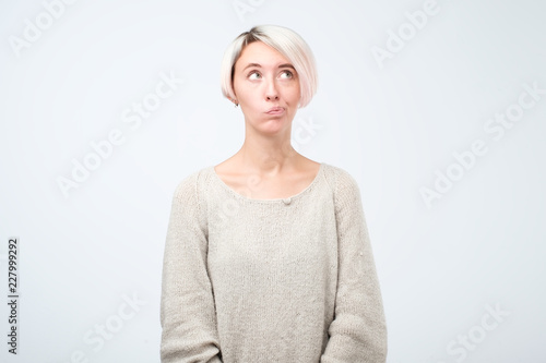 European girl with dyed hair looking away, having doubtful and indecisive face expression, pursuing her lips photo