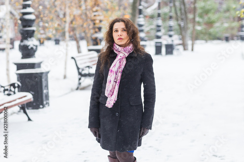 City, season and people concept - Beautiful young woman in black coat and pink scarf in winter street © satura_