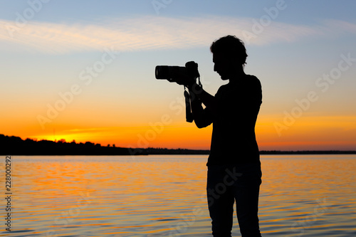Young male photographer taking photo of riverside sunset with professional camera outdoors © New Africa