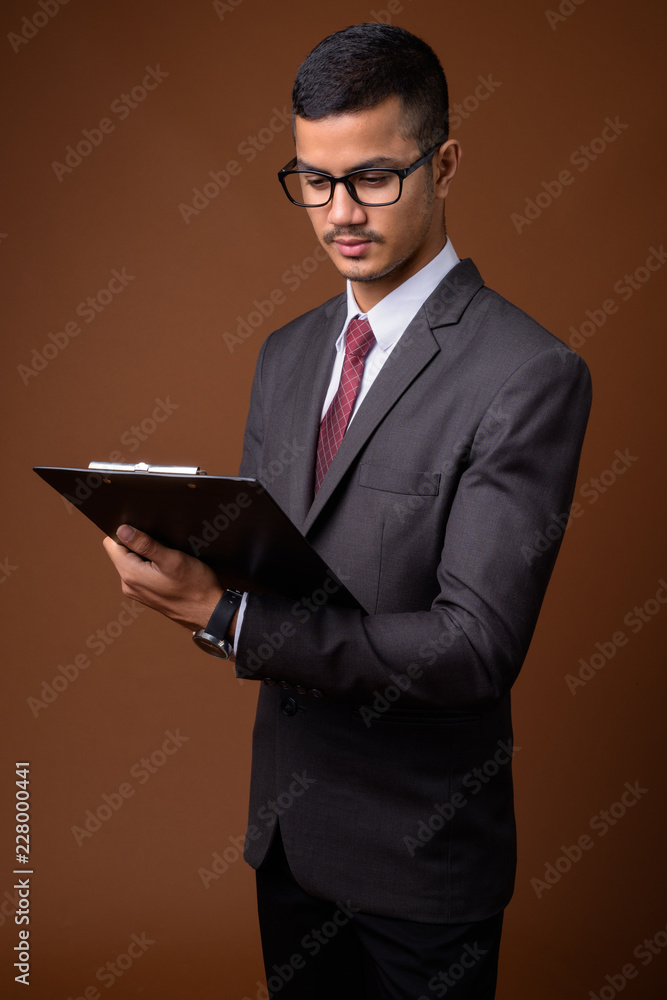 Young multi-ethnic Asian businessman against brown background Young multi-ethnic Asian businessman against brown background