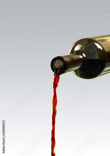 Red wine pouring from bottle on white