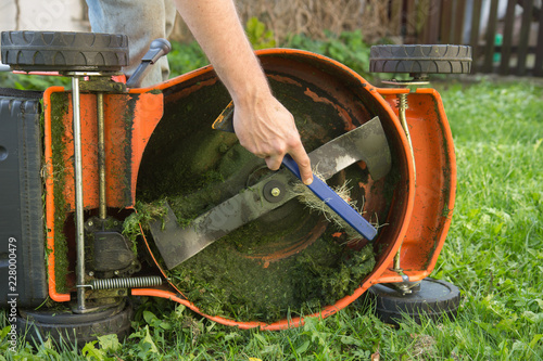 Man's hand with brush cleaning lawn mower