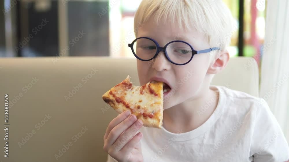 Schoolboy eats in the school cafeteria. The boy is holding a slice of margarita pizza. Bites off. Cheese pulls. Break, lunch Schoolboy eats in the school cafeteria. The boy is holding a slice of margarita pizza. Bites off. Cheese pulls. Break, lunch