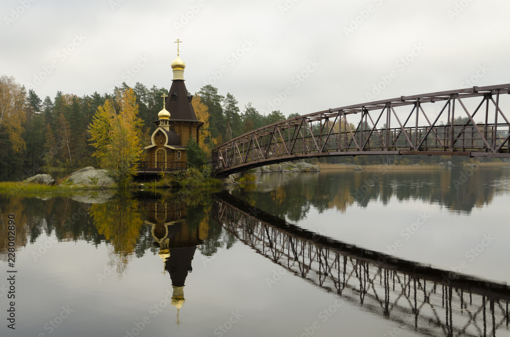 Fototapeta premium Landscape. View of Lake Vuoksa on an autumn day. There is an Orthodox church of St. Andrew the First-Called on an island in the middle of the lake. There is a bridge to the island.