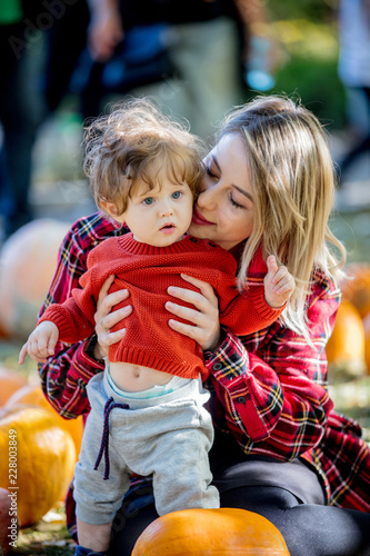 Young mother with a child on a lawm with a pumpkins. Autumn season time. photo