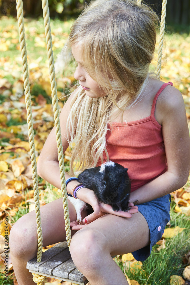 Cute child girl sitting on swing in garden and playing with guinea pig pet animal Cute child girl sitting on swing in garden and playing with guinea pig pet animal