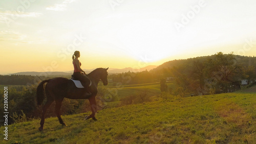 AERIAL: Flying along young woman riding her beautiful brown horse at sunrise. © helivideo