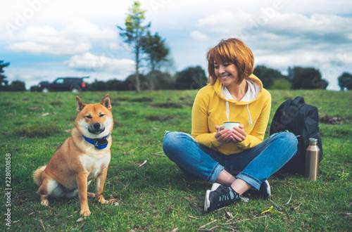 Happy smile girl holding in hands cup drink, japanese dog shiba inu on green grass in outdoors nature park, woman hipster and dogs friends, friendship lifestyle relax recreation concept © A_B_C