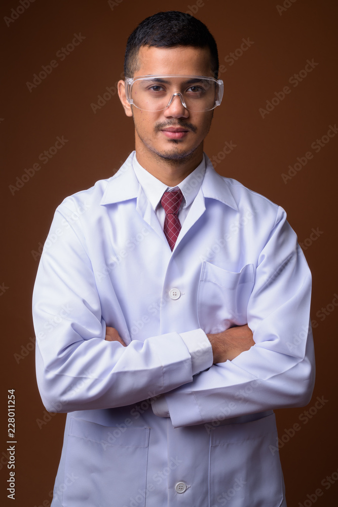 Young multi-ethnic Asian man doctor against brown background Young multi-ethnic Asian man doctor against brown background