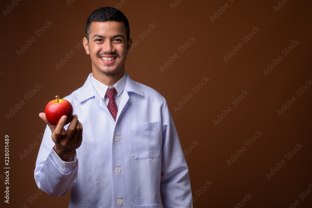 Young multi-ethnic Asian man doctor against brown background Young multi-ethnic Asian man doctor against brown background