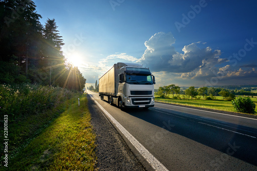 White truck arriving on the asphalt road in rural landscape in the rays of the sunset photo