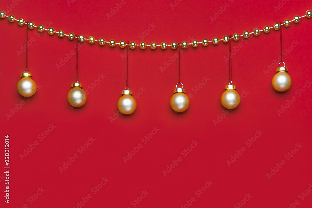 Six small matte golden-coloured Christmas ornament hanging on a row decorated by shiny golden-coloured Christmas beads wreath on red background in studio light Six small matte golden-coloured Christmas ornament hanging on a row decorated by shiny golden-coloured Christmas beads wreath on red background in studio light