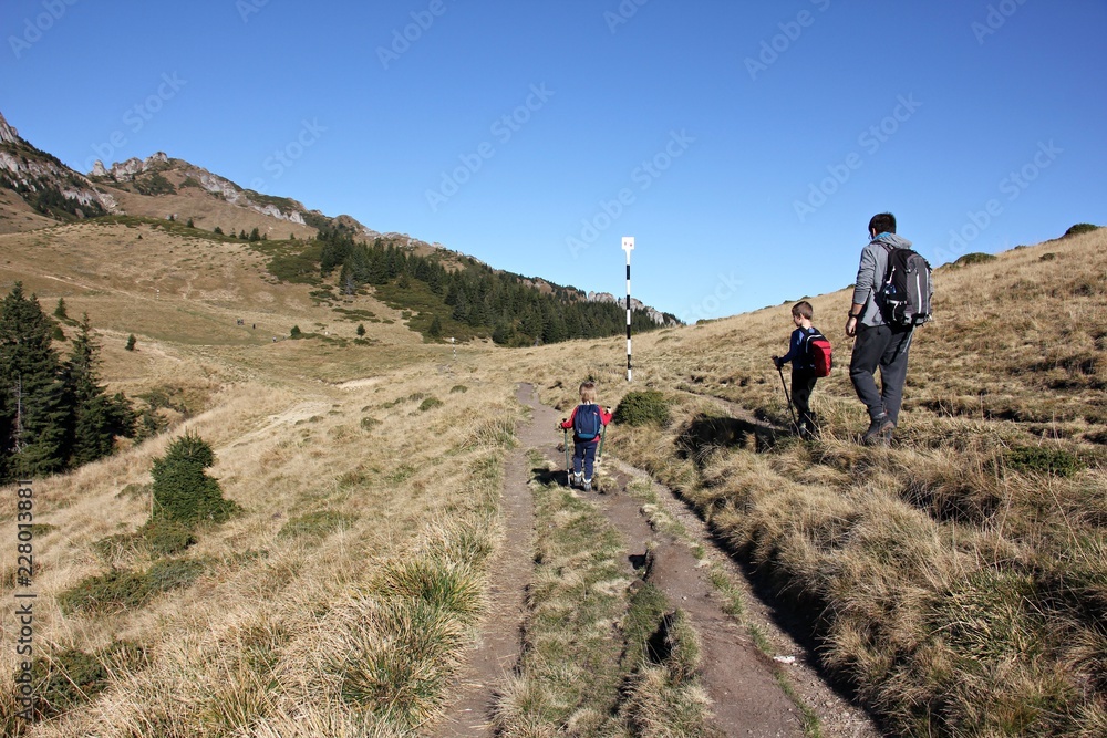 Family: father and two children, trekking on a mountain trail. 