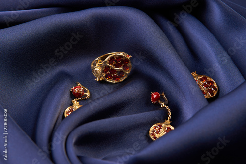 Rubies ring, necklace and earrings on blue silk background with copy space. Beautiful precious women's gold jewelry, close-up. 