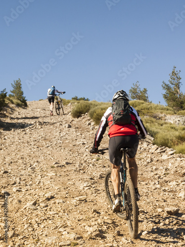Women and mountain biking man riding on bikes in the mountains forest landscape. MTB track cycling couple enduro flow trail. Outdoor sports activity. Hard and steep climb