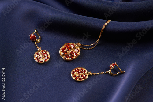 Ruby necklace and earrings on blue silk background with copy space. Beautiful precious women's gold jewelry, close-up. 