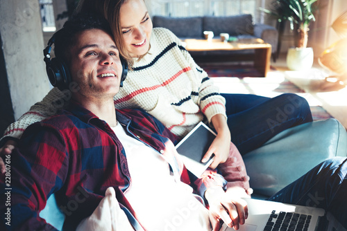 Happy couple at home. Husband and wife sitting on the couch together and watching TV series on laptop, listening music and reading books. Bright loft apartment