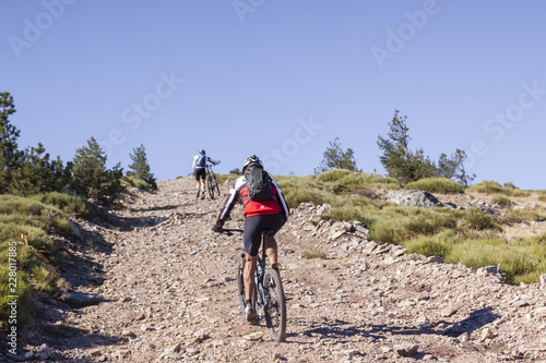 Women and mountain biking man riding on bikes in the mountains forest landscape. MTB track cycling couple enduro flow trail. Outdoor sports activity. Hard and steep climb