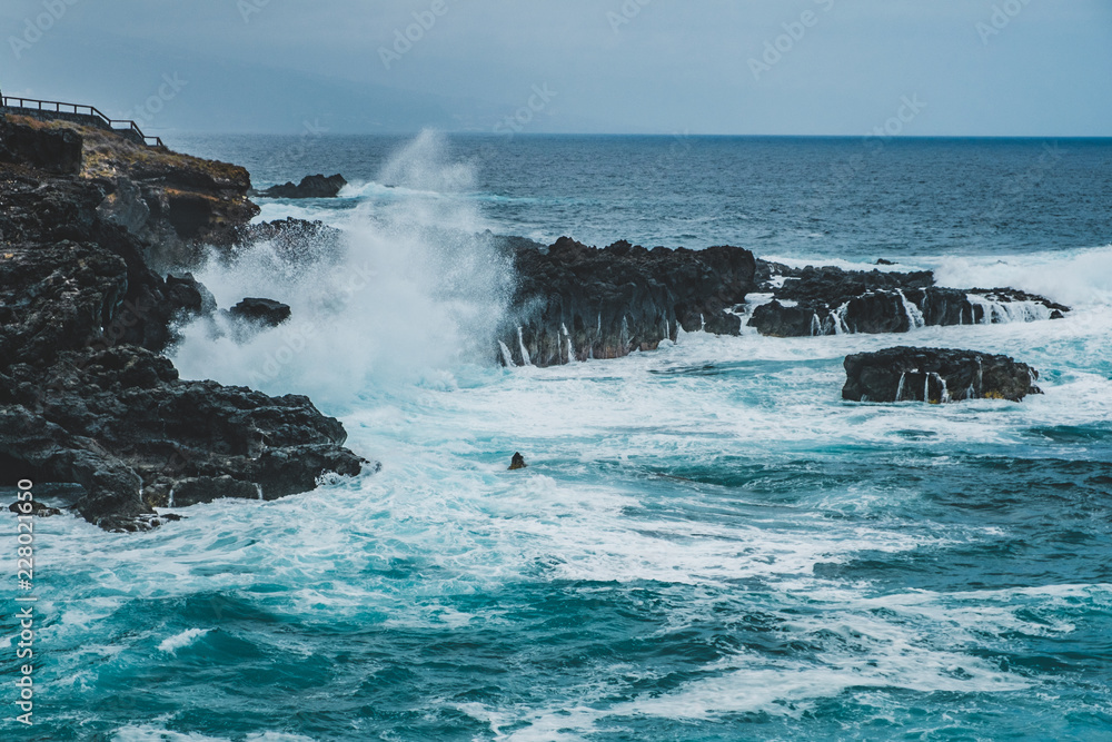 ocean waves crashing against black rocks on coast